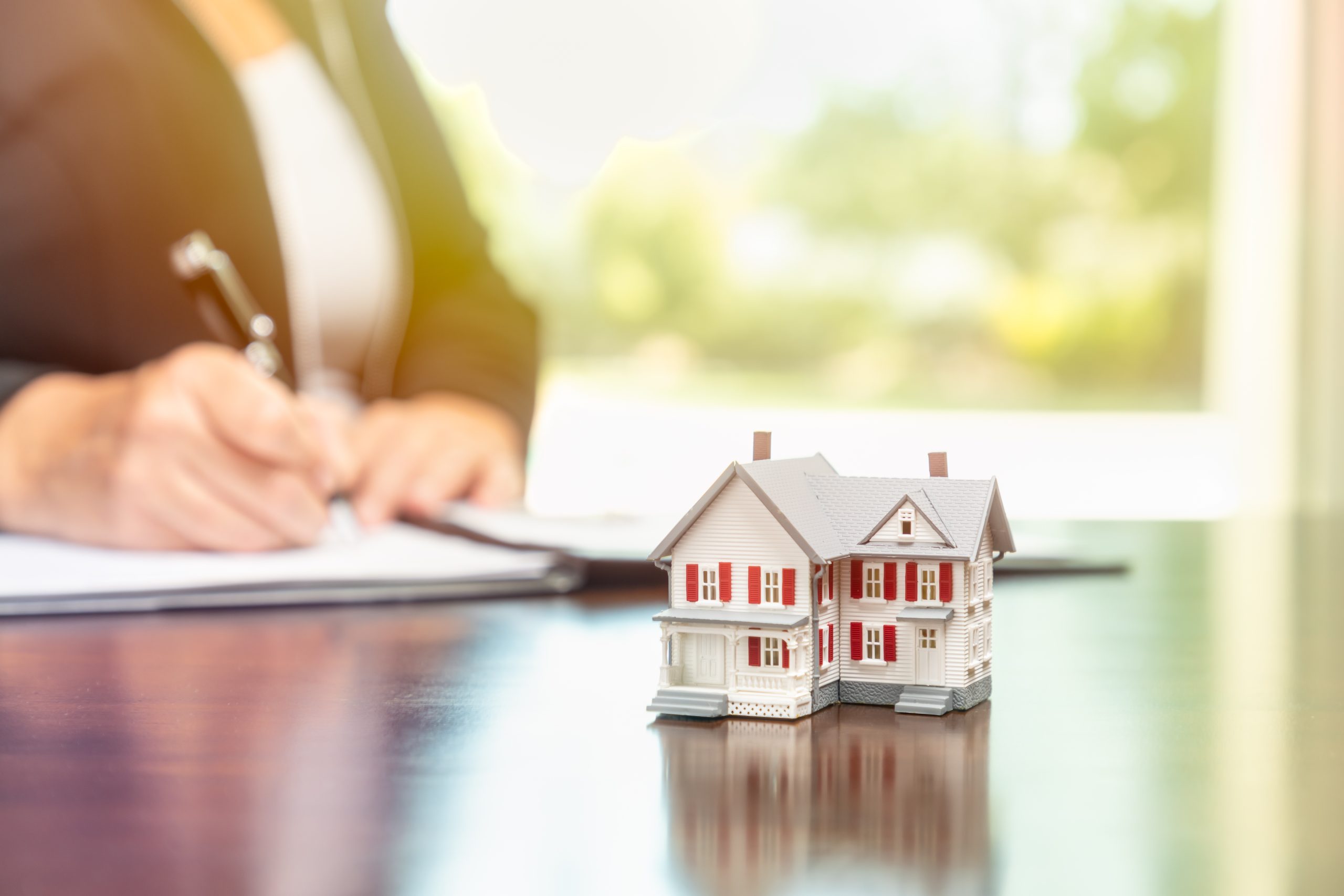Woman signing real estate contract papers with small model home in front.